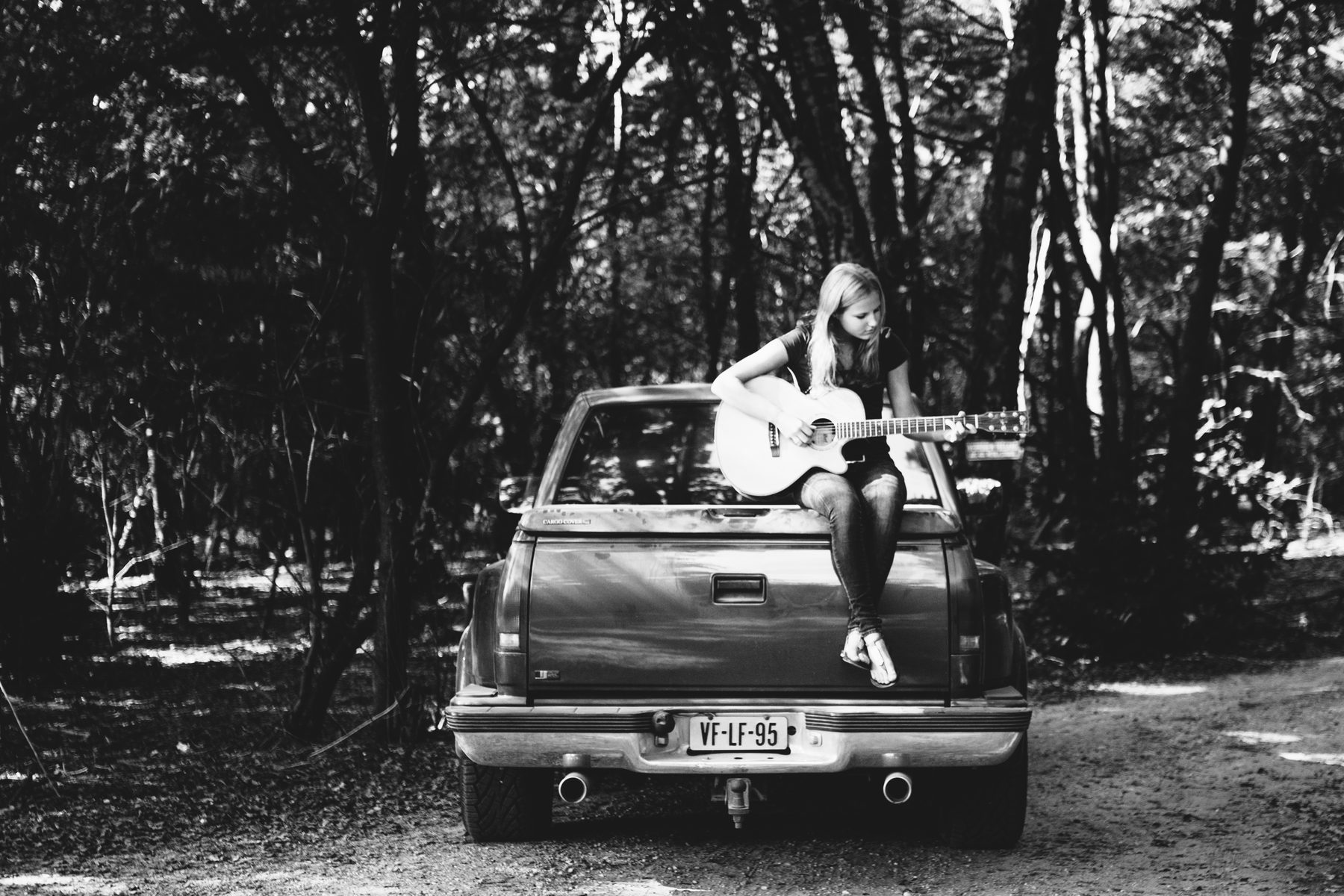Meisje met een akoestische gitaar op de laadklep van een pick-up